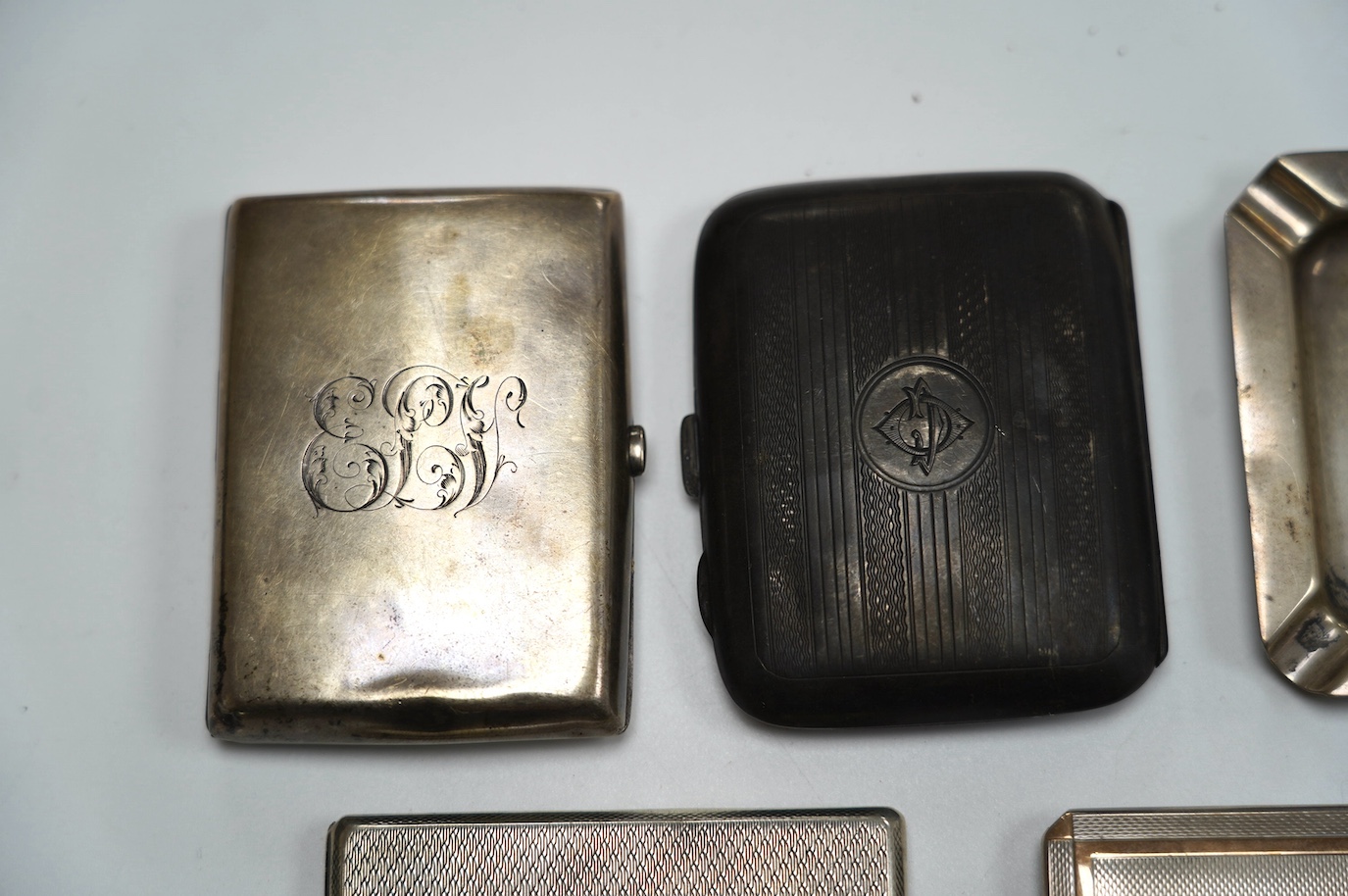 A George VI engine turned silver cigarette case, with yellow metal band, London, 1938, 11.4cm, four other silver cigarette cases and a silver ashtray, gross weight 16.8oz. Condition - poor to fair